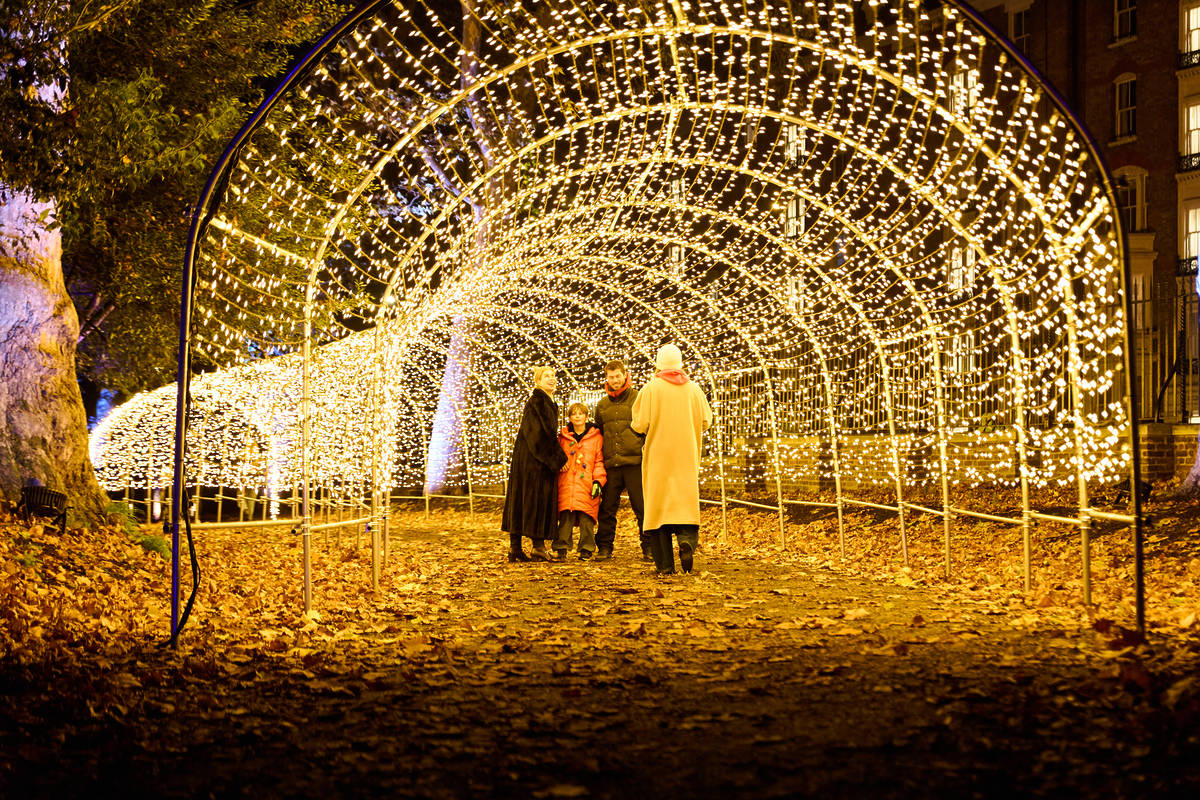 people stood at the entrance of a tunnel of fairy lights at night