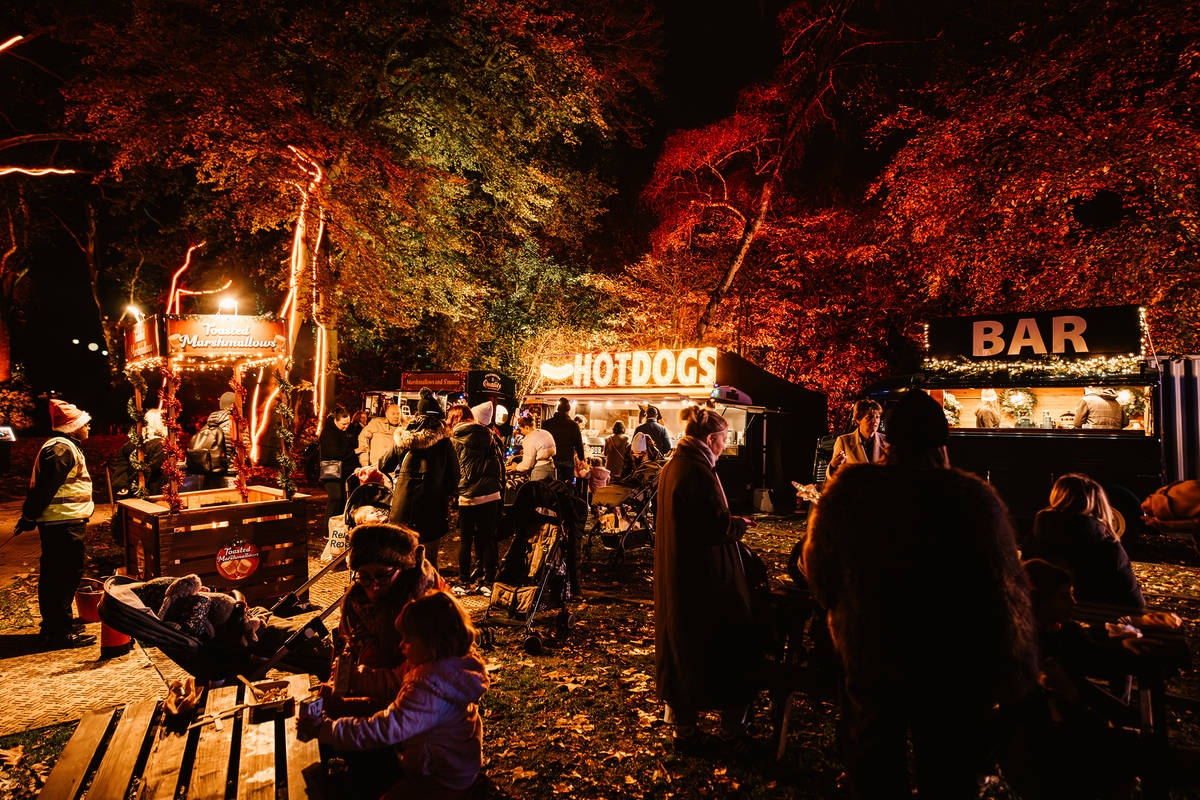 a christmas market in the evening, with people milling about enjoying street food from the stands