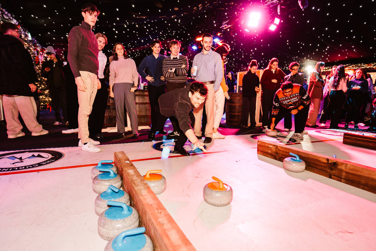 people enjoying a session of curling, standing around chatting and watching, or leaning down to push a huge curling stone across the ice