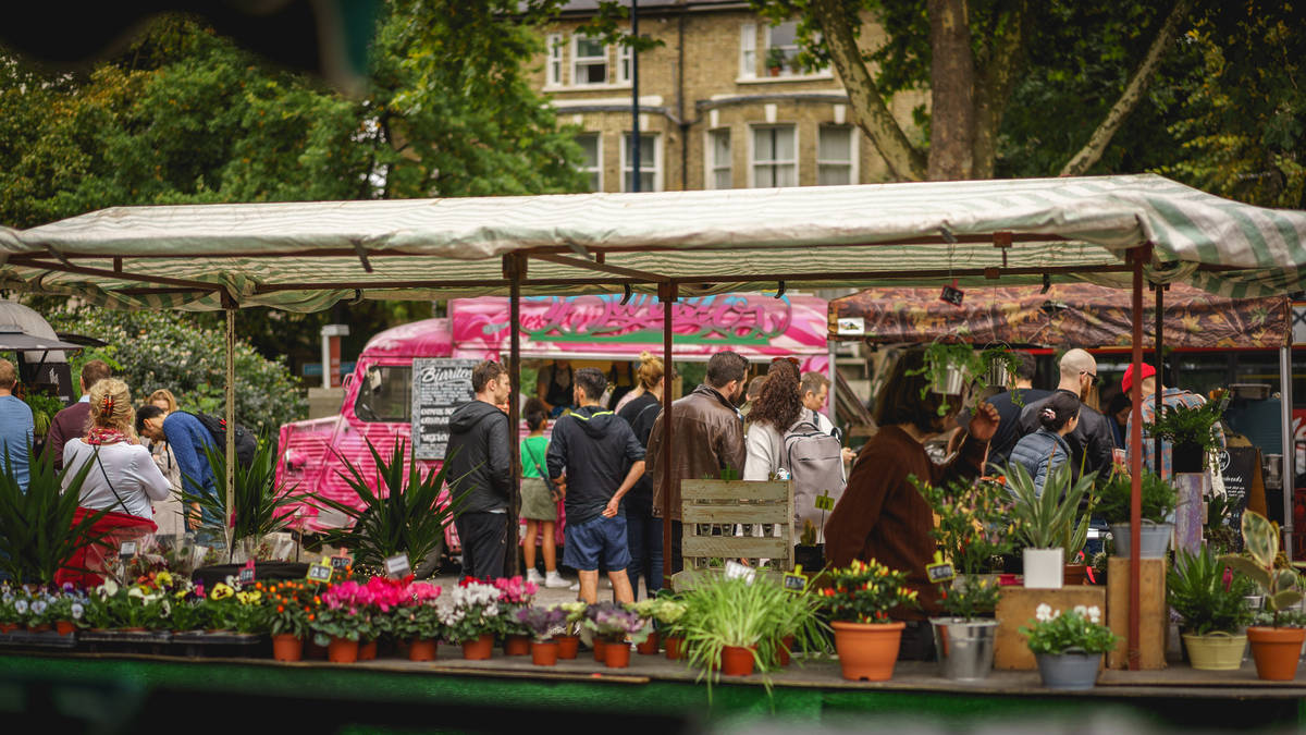 People shopping at Brockley Market, with a stand full of flowers and plants in the foreground