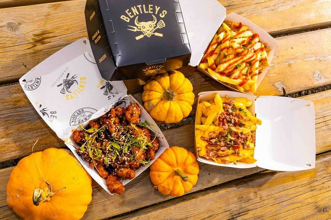 Open boxes of loaded fries and chicken, amongst some small pumpkins.
