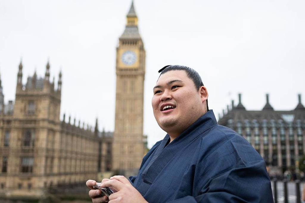 A sumo wrestler stand smiling in front of Big Ben and Houses of parliament in London