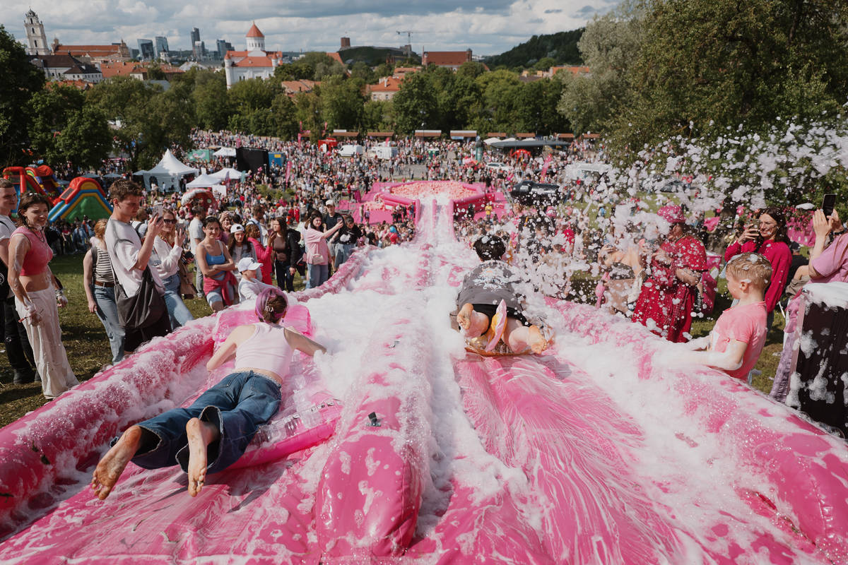 Two large pink slip and slides in the centre of a crowd with two people sliding down them
