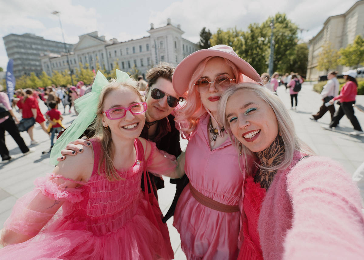 Four people dressed in pink outfits smile into the camera