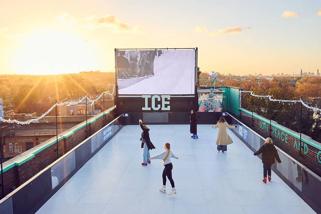 gente patinando en una pista de hielo en una azotea, con vistas a londres