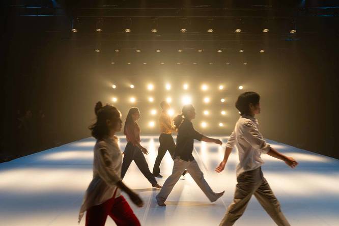 Dancers walking on stage to the right, illuminated by strong back lighting