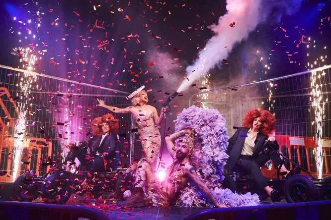 A troupe of drag and cabaret performers celebrate on stage, with confetti in the air