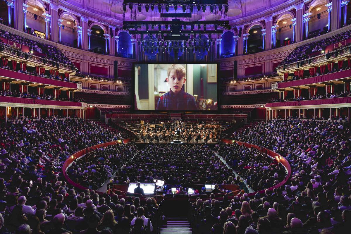 Wide shot of the inside of the Royal Albert Hall with a still from "Home Alone" on a big screen with the audience watching