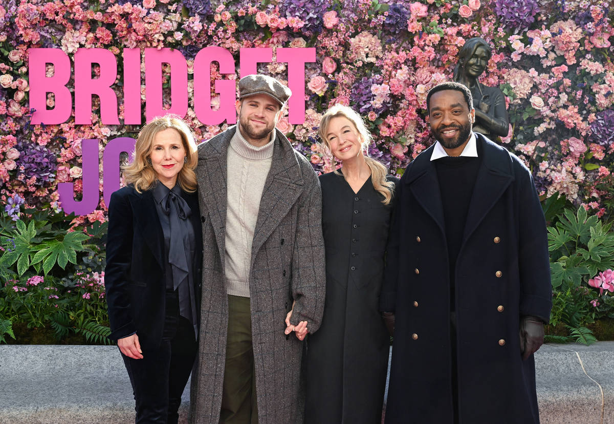 Renée Zellweger and some of her bridget jones co-stars posing in front of a floral display celebrating the new bridget jones statue
