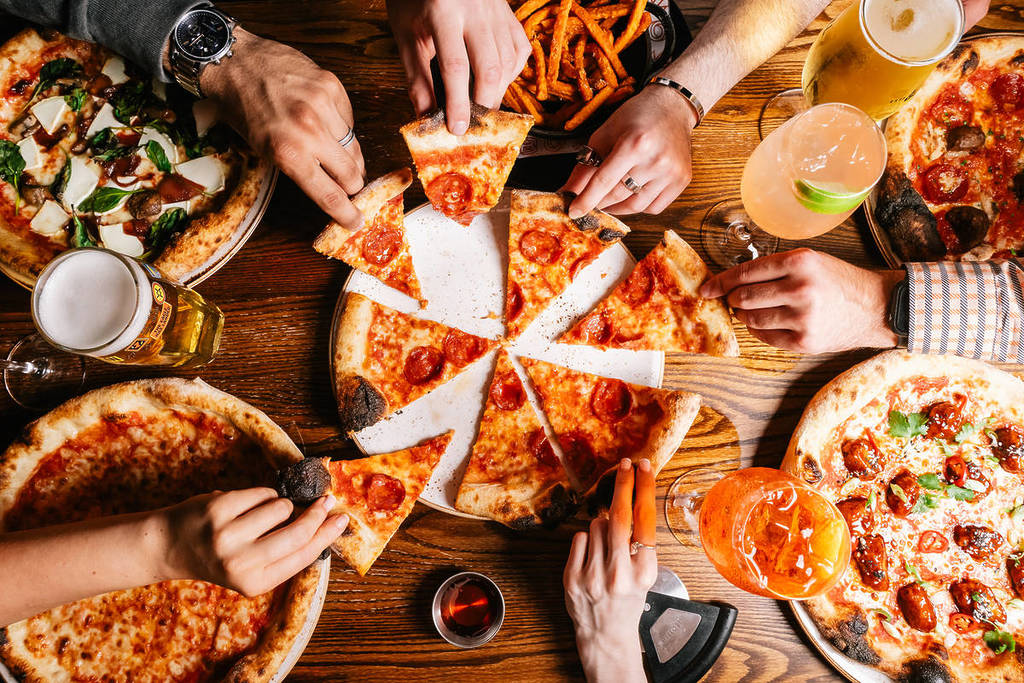 persone che si avvicinano a fette di pizza su un tavolo