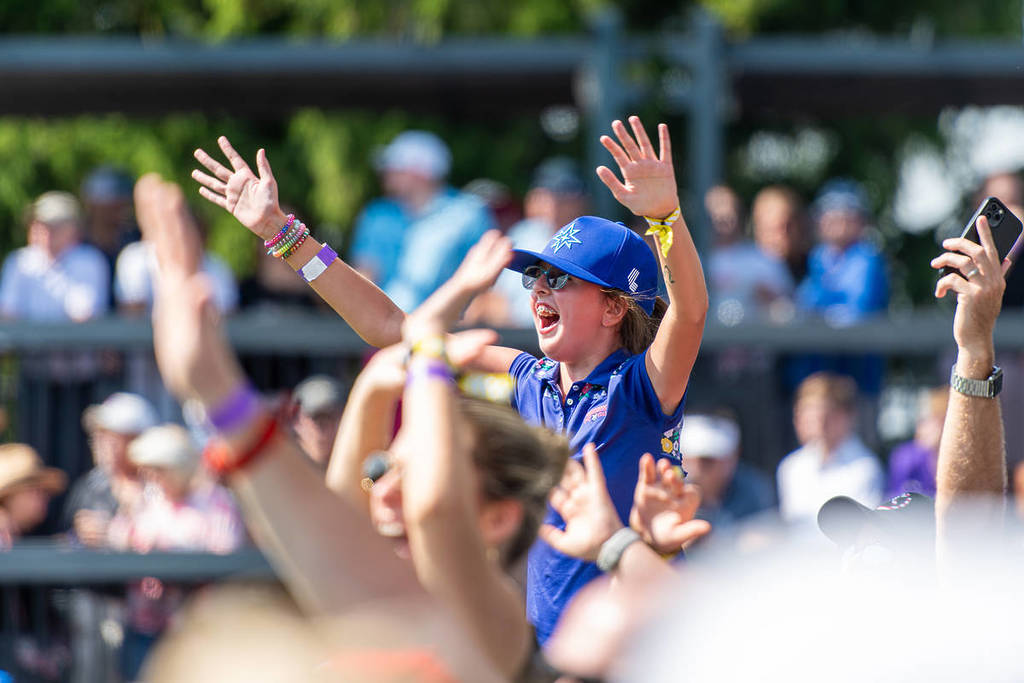 a kid on someones shoulders cheers with his hands in the air at LIV Golf
