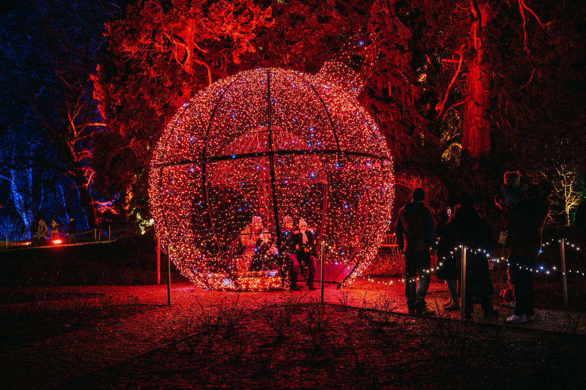 a giant glittering red christmas bauble light installation, with people posing inside for a photo
