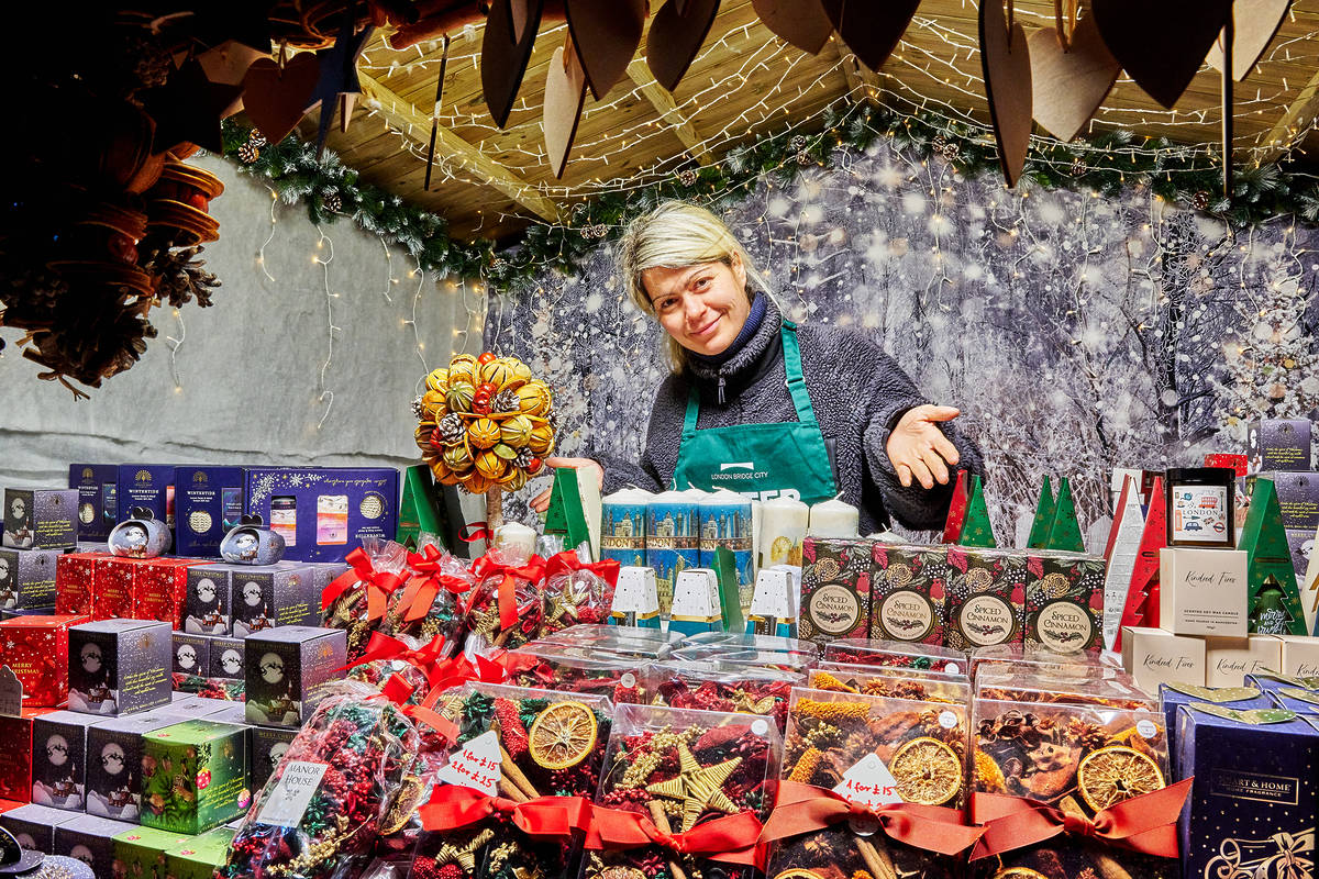 a market trader behind a counter gesturing at their array of christmas goods