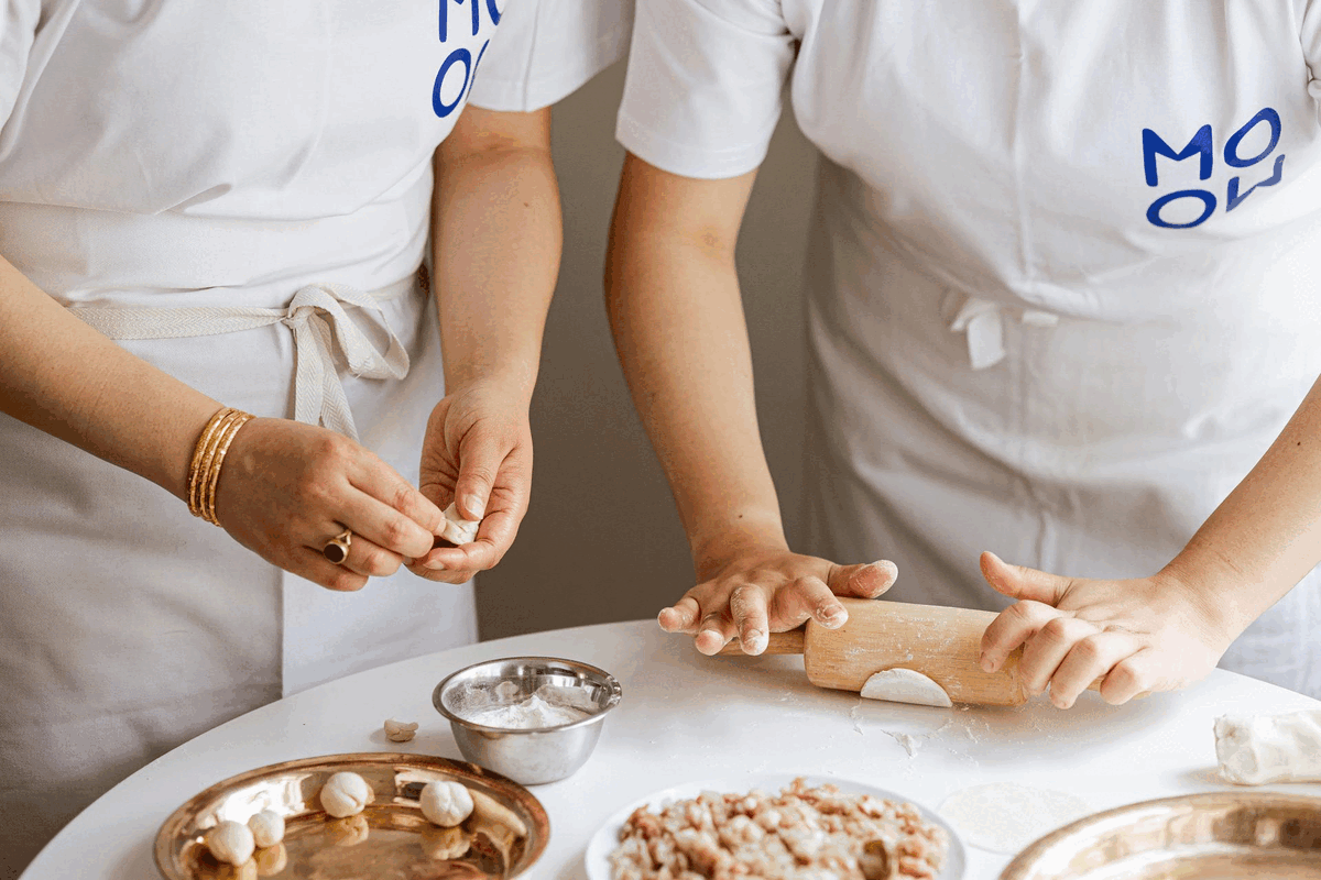 two people in white outfits rolling out and filling momo dumplings
