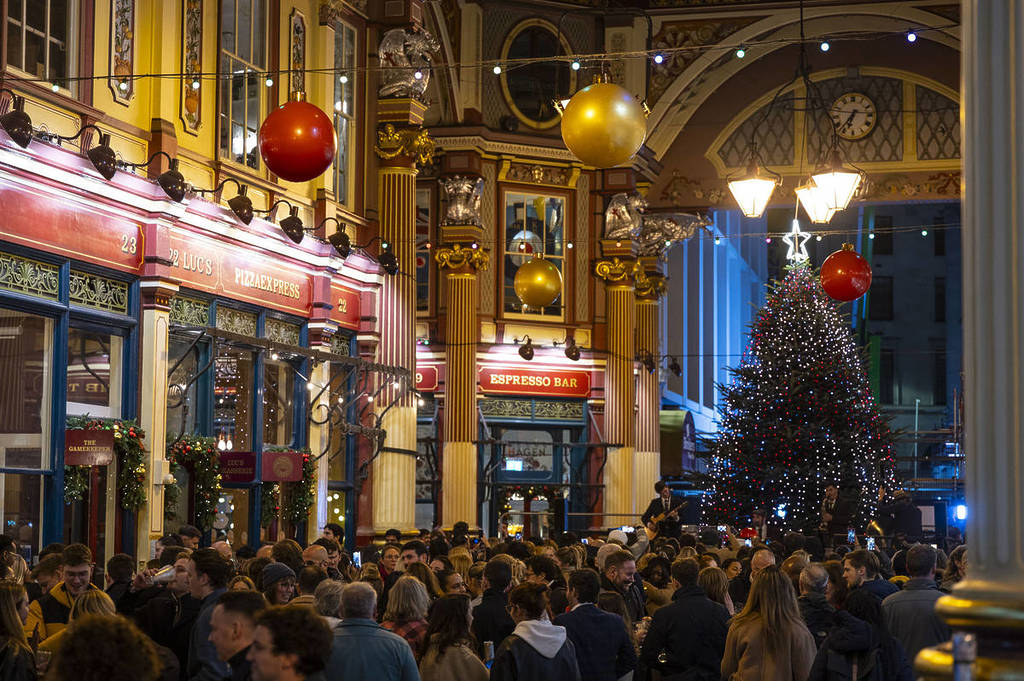 people thronging around leadenhall market beneath christmas decorations, with a large christmas tree looming overhead