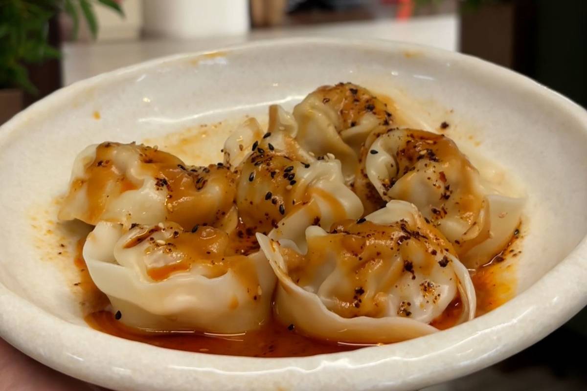 5 or 6 wontons lie of a bowl covered in a reddish sauce