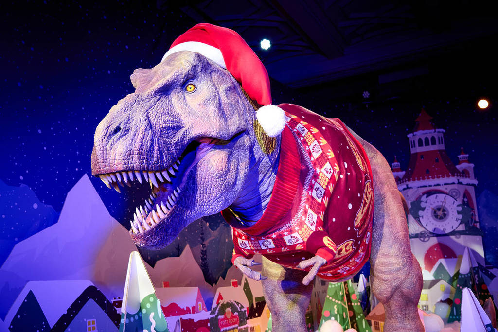 a fearsome but festive t rex animatronix wearing a christmas jumper and a santa hat