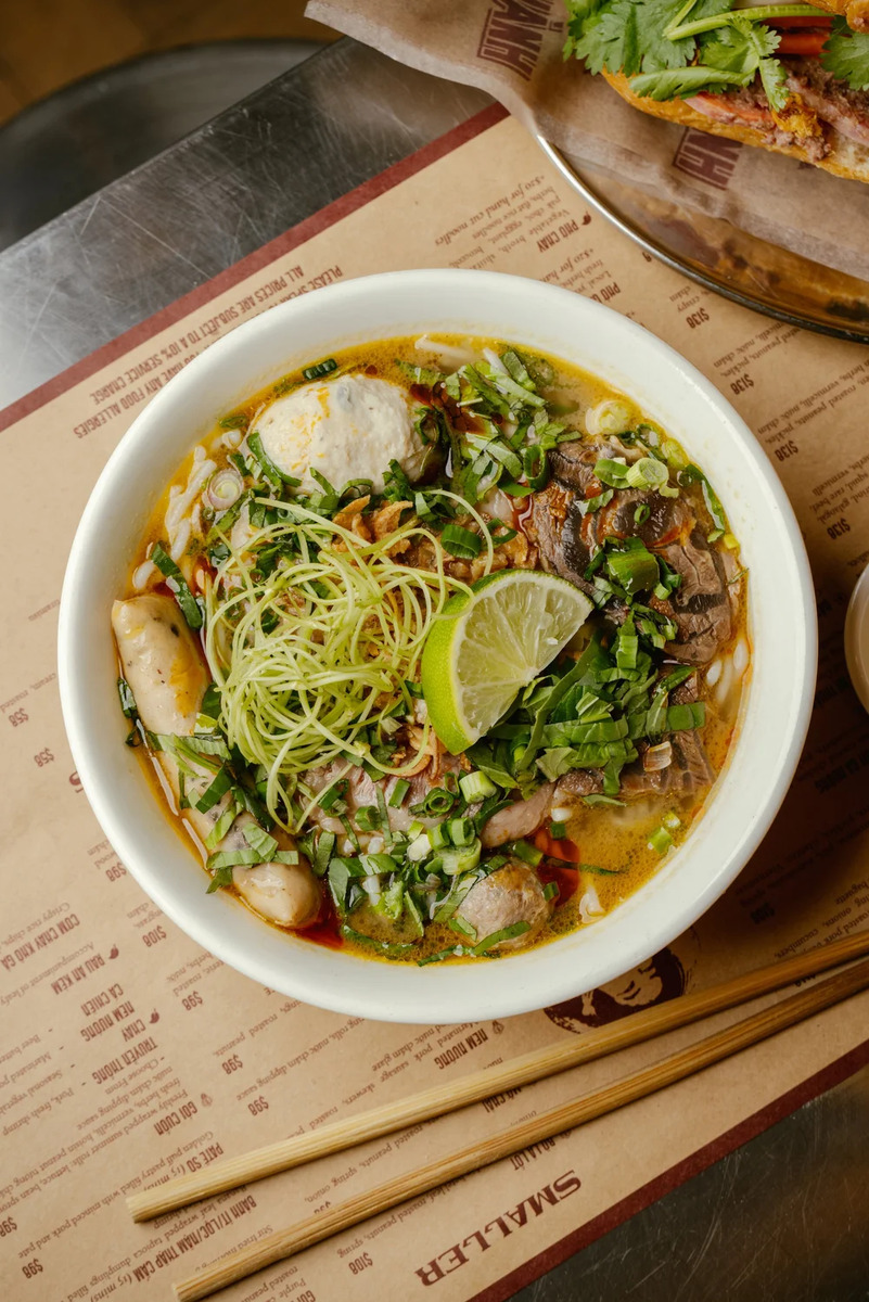 a bowl of beef noodle soup with bright green toppings and garnishes
