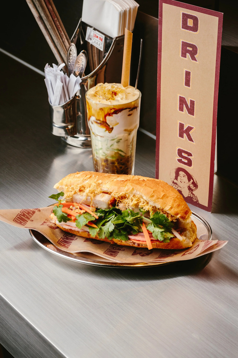 a banh mi next to an iced vietnamese coffee