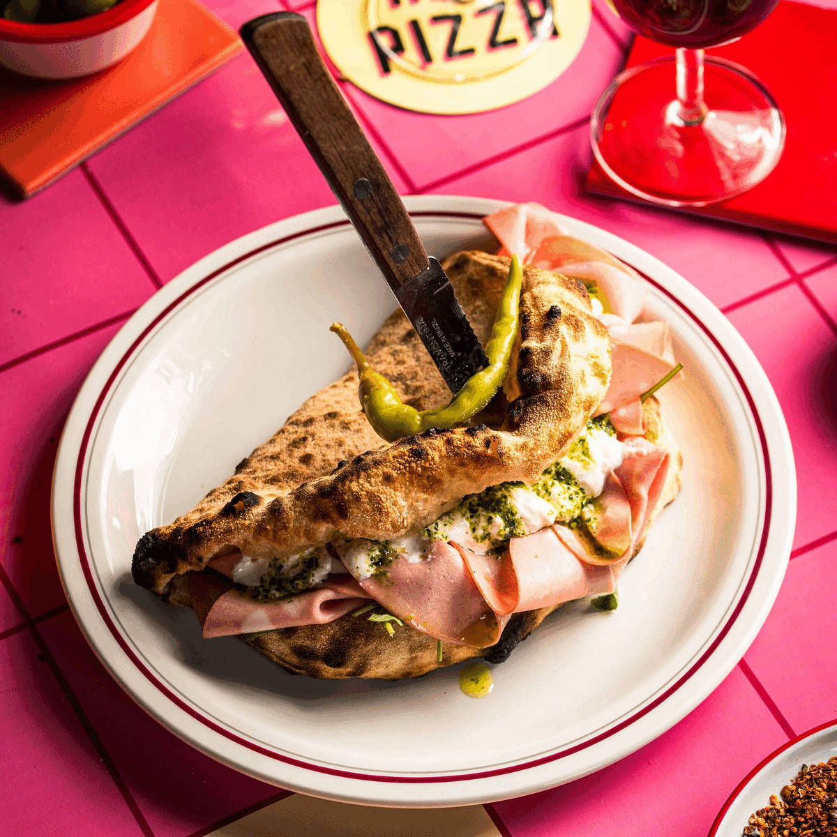 a pizza sandwich made from pizza dough wrapped in half around fillings. A knife is stabbed into it, holding it all together