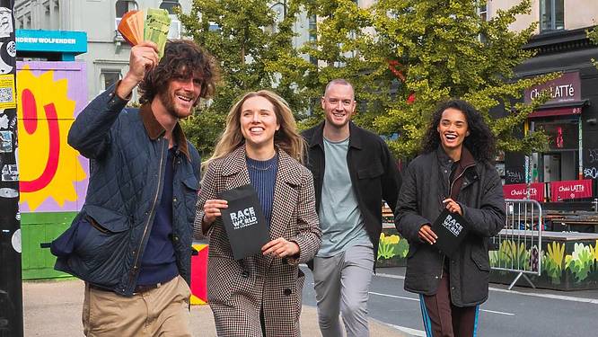 four adults laugh and celebrate while holding Race Across The World pamphlets