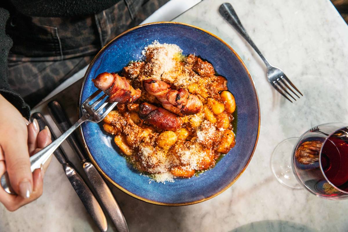 a blue bowl filled with a portion of gnocchi and ragu, topped with crispy pigs in blankets