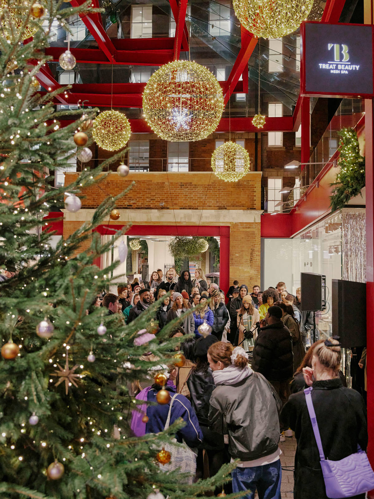 people milling about and watching a live performance in islington square underneath suspended christmas lights with a christmas tree in the foreground