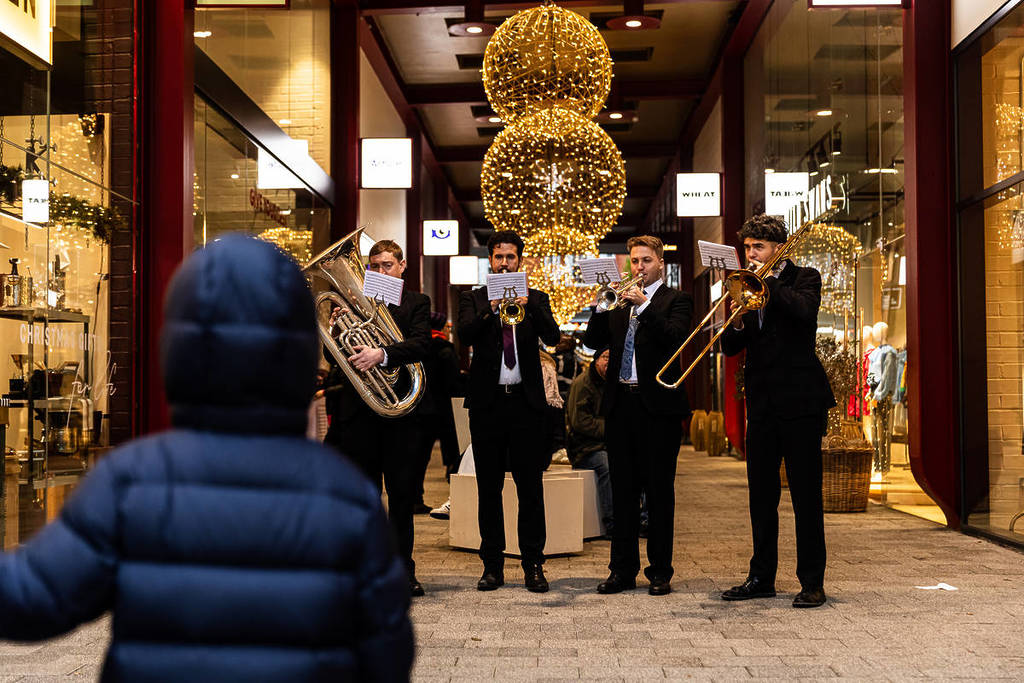 a child stood watching a brass band perform in front of christmas decorations