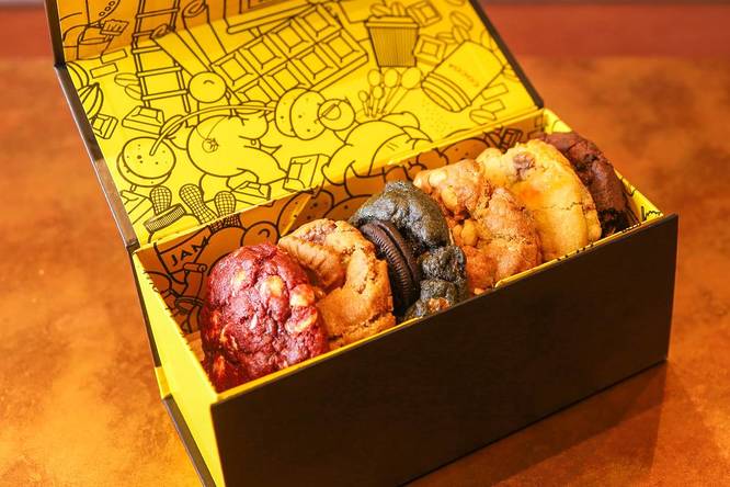 a box with a yellow patterned interior filled with chunky cookies in a variety of flavours