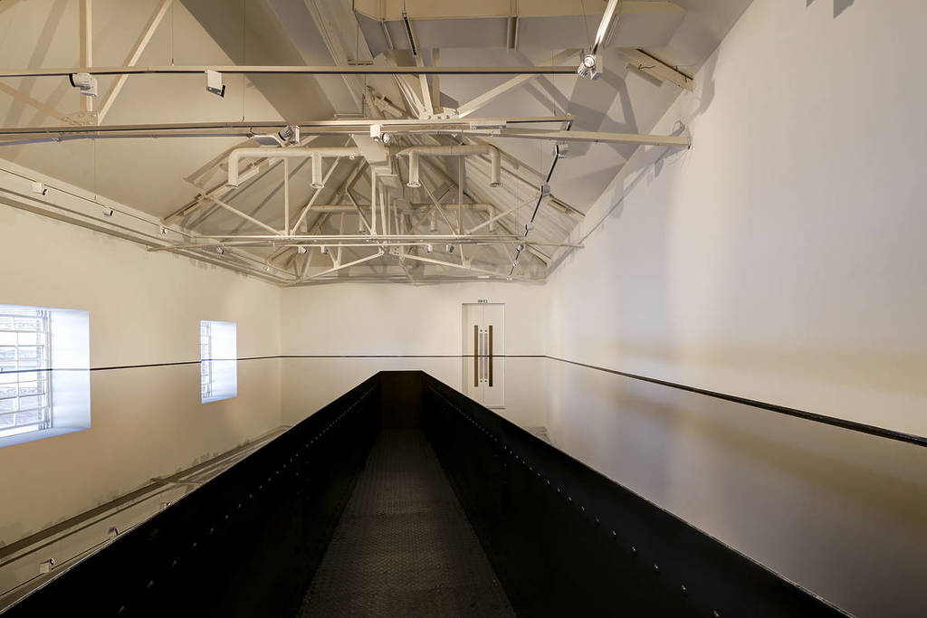 a walkway leading into a room that has been flooded with oil, reflecting everything around it on its still surface