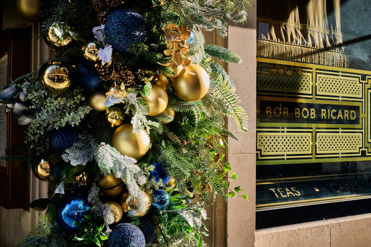 a close up of blue, green, and gold christmas decorations and baubles framing a doorway, with the window visible to the side, emblazoned 'bob bob ricard'.