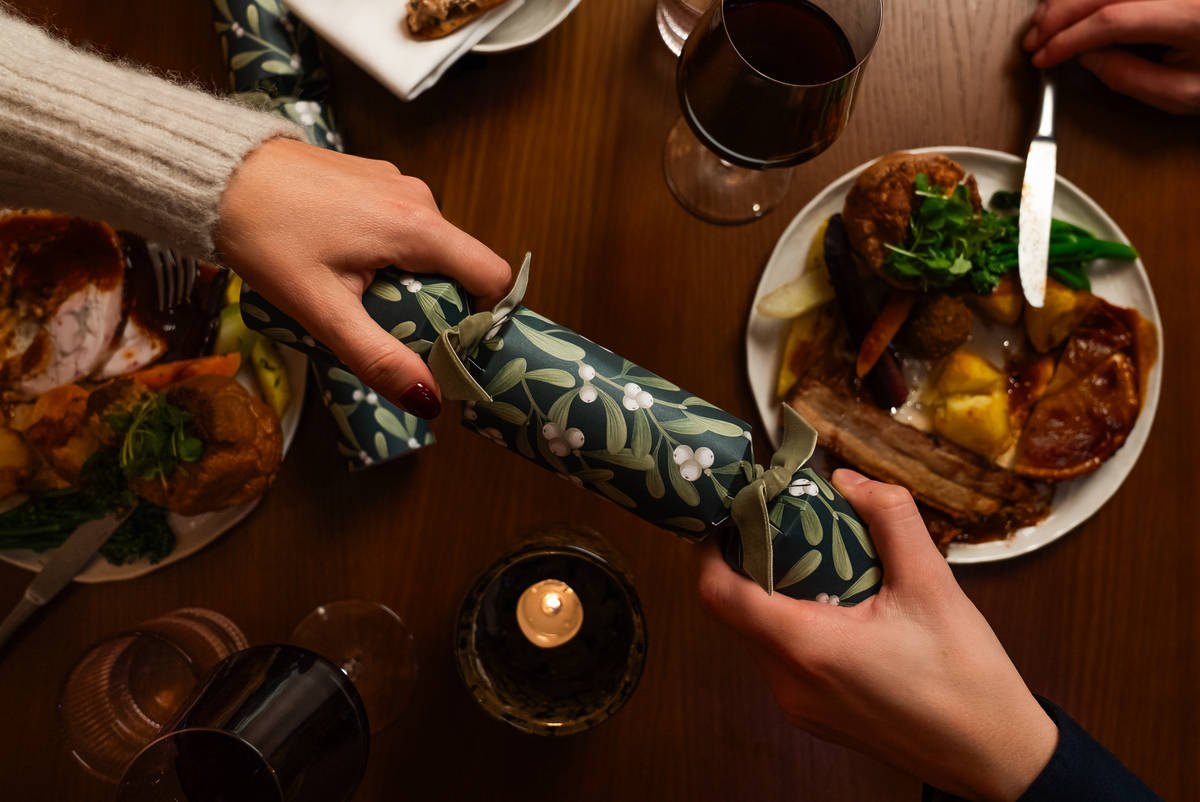 hands holding either end of a christmas cracker over a table laid with two christmas meals