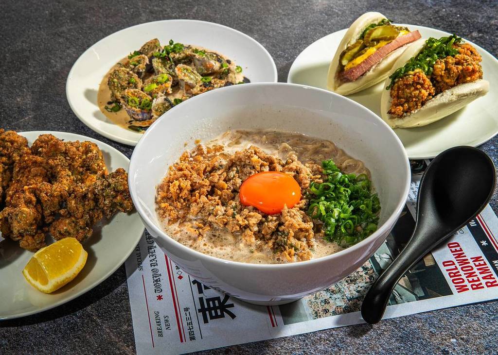 a bowl of ramen in the middle of a variety of japanese starter dishes, ranging from fried chicken to chicken buns
