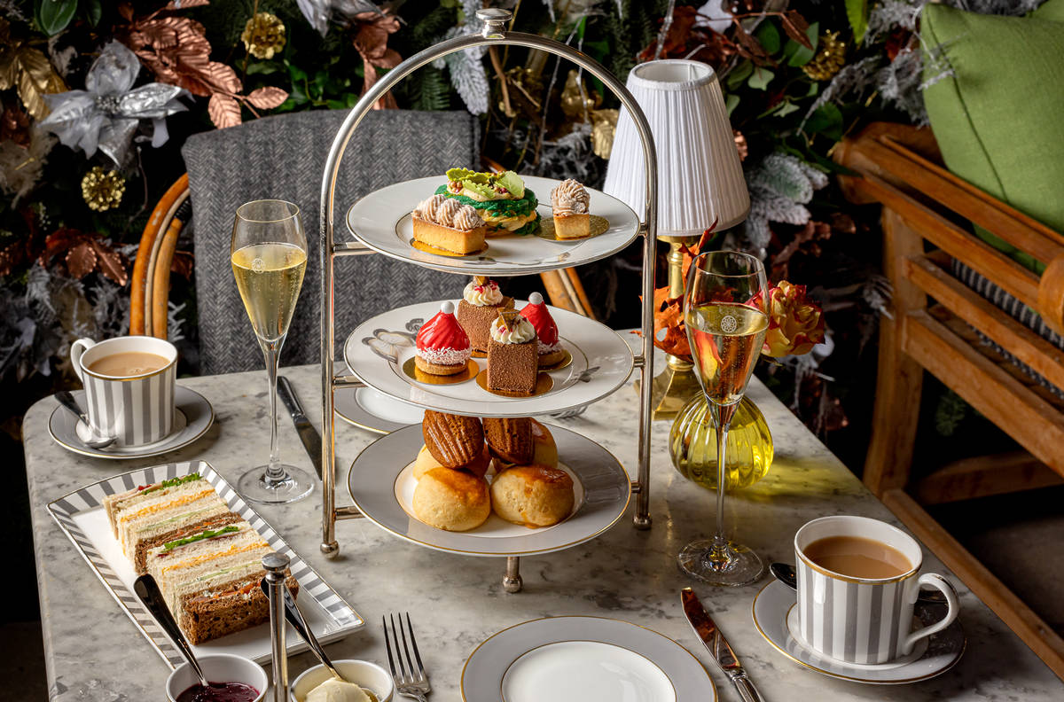a winter themed afternoon tea spread on a table, with a tiered tray of food, crockery, and glasses of champagne and mugs of tea