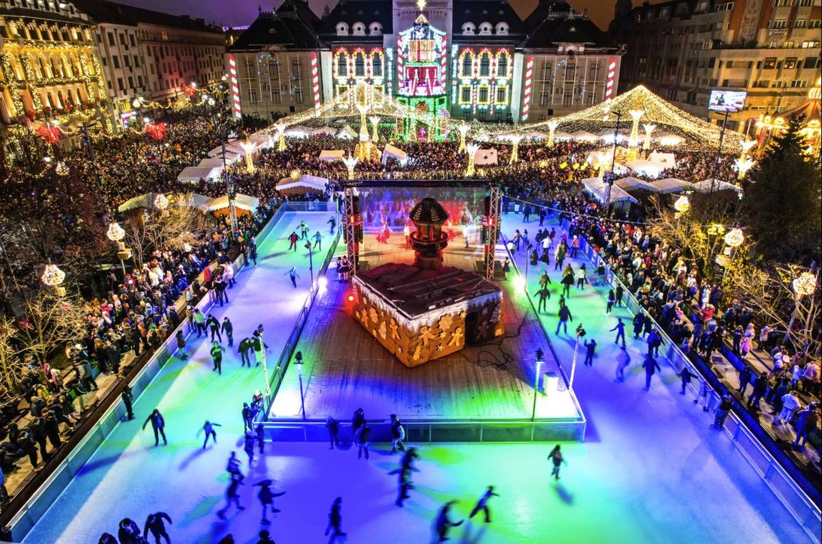 large ice rink in the middle of a city square with christmas lights and markets around
