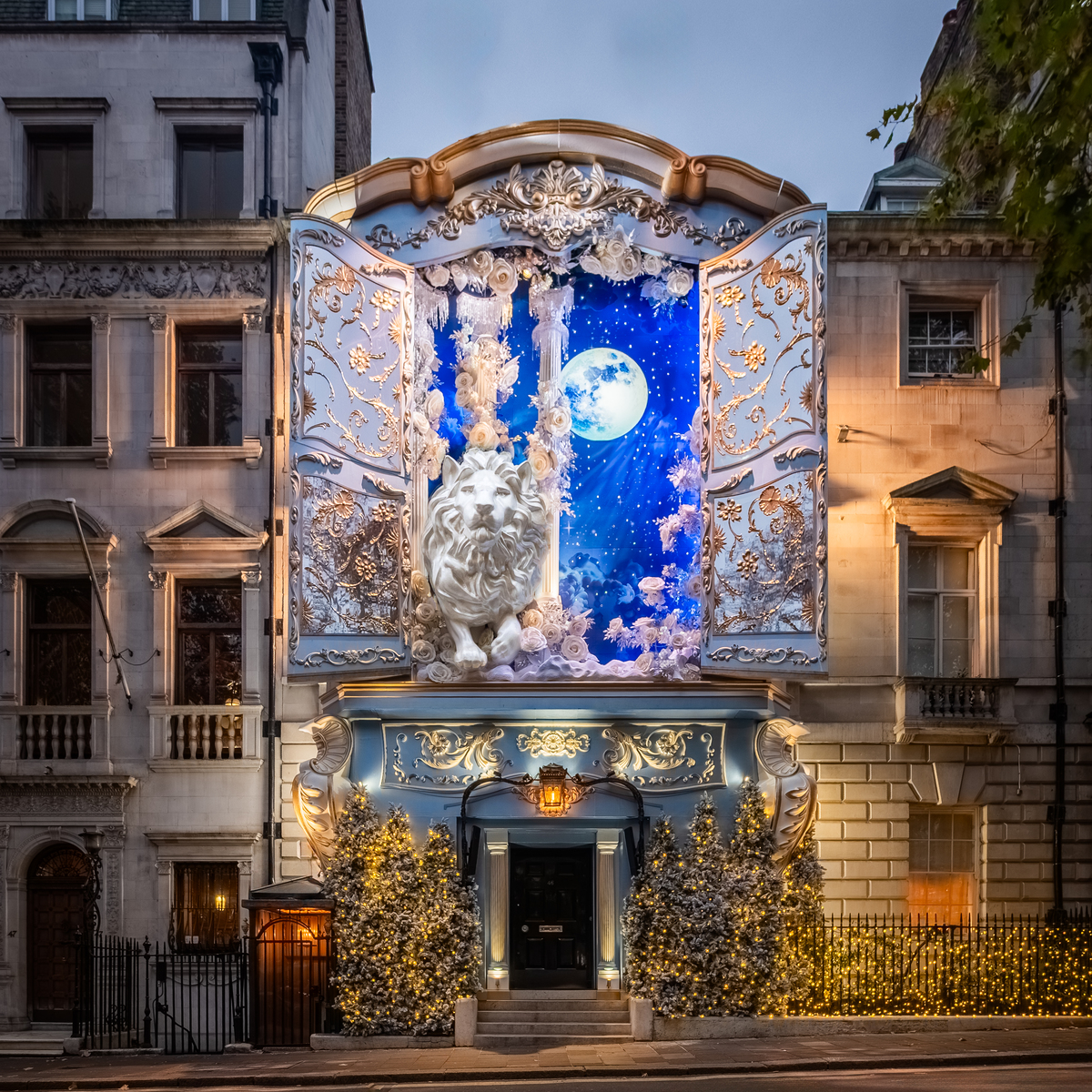 a narnia-inspired wintry scene taking over the side of a building in london, featuring a lion gazing out from open wardrobe doors, amidst a snowy scene of trees and icicles