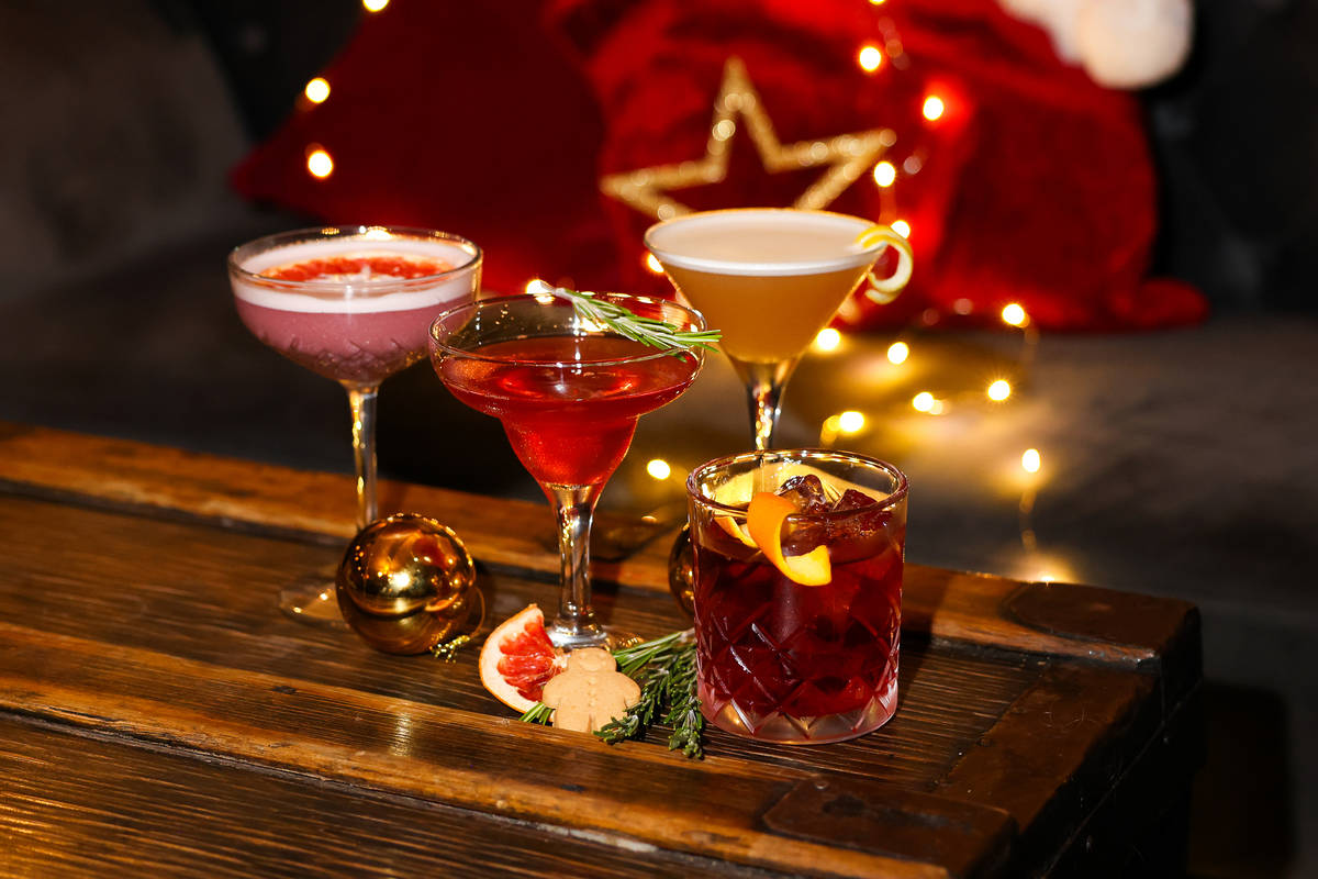 four Christmas cocktails arranged on a table around some gingerbread, rosemary, and a frapefruit slie