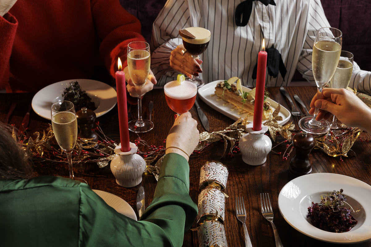 glasses of wine and cocktails being cheersed over a table full of christmas dishes and decoration