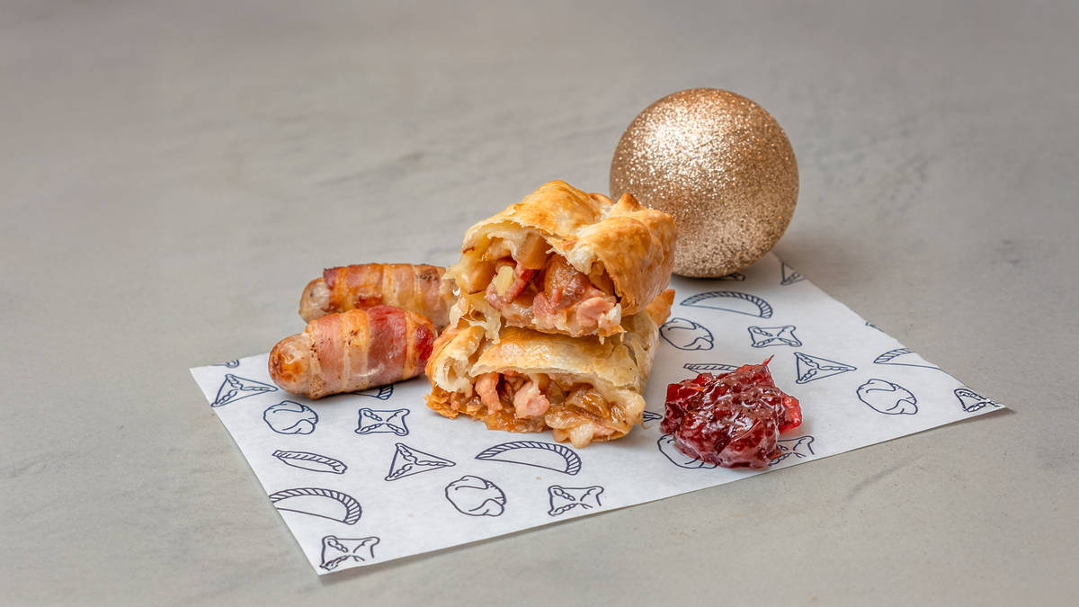 a pigs in blanket empanada cut in half and stacked with the fillings shown to the camera, with some pigs in blanket next to it, and some cranberry sauce