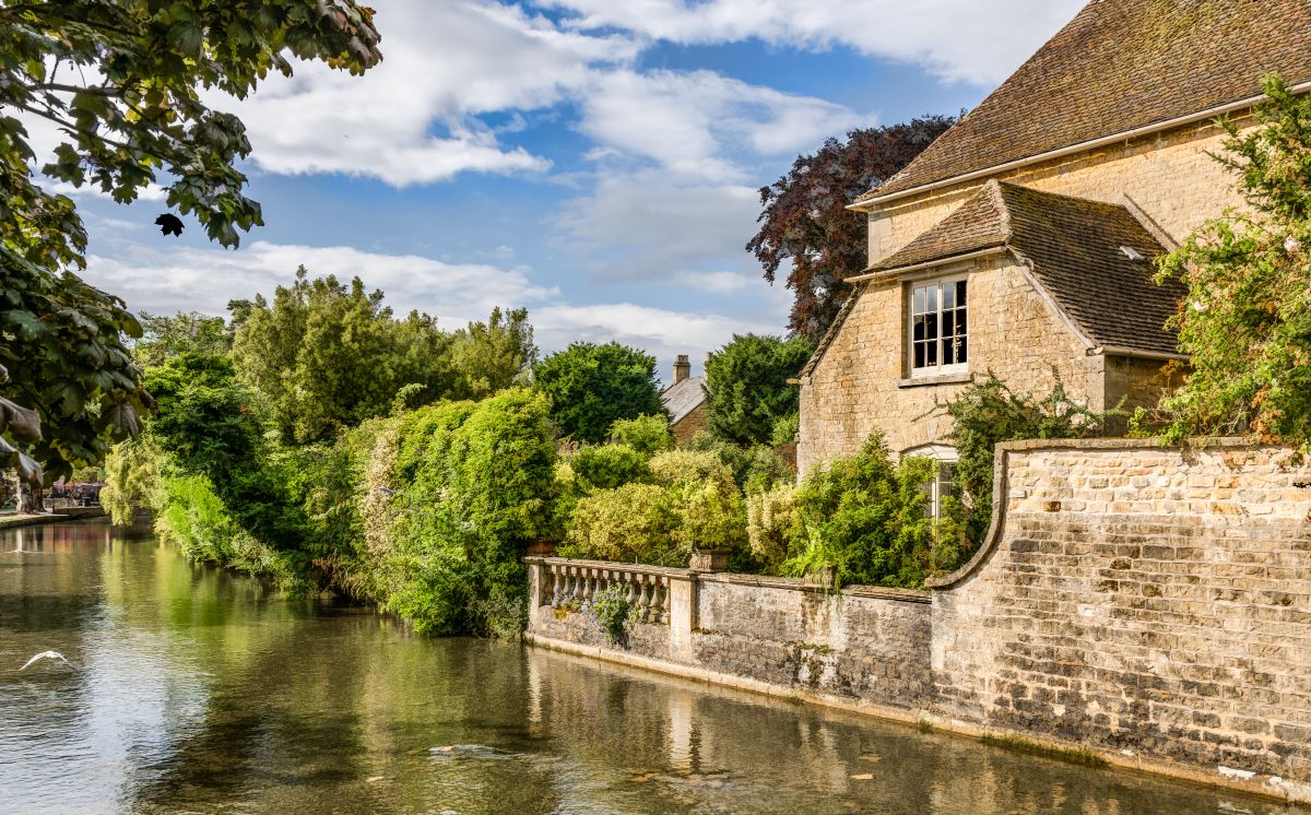 The River Windrush surrounded by greenery and a goldenstone building