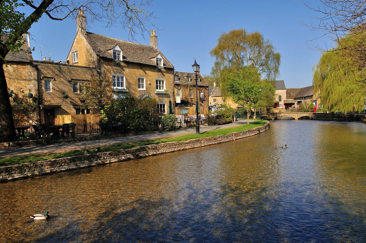 Houses on the riverbank in Bourton-on-the-Water under a bright blue sky