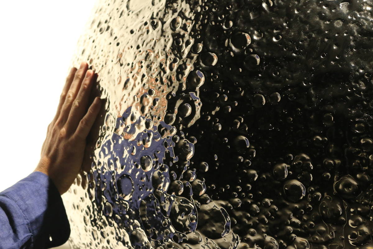 a hand reaching out to touch a large detailed sculpture of the moon made from stainless steel