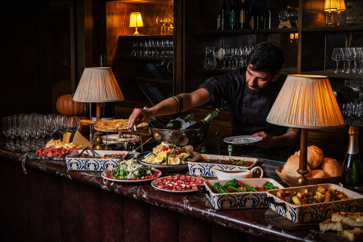 a chef reacing out over a buffet of food to add a finishing garnish to a dish