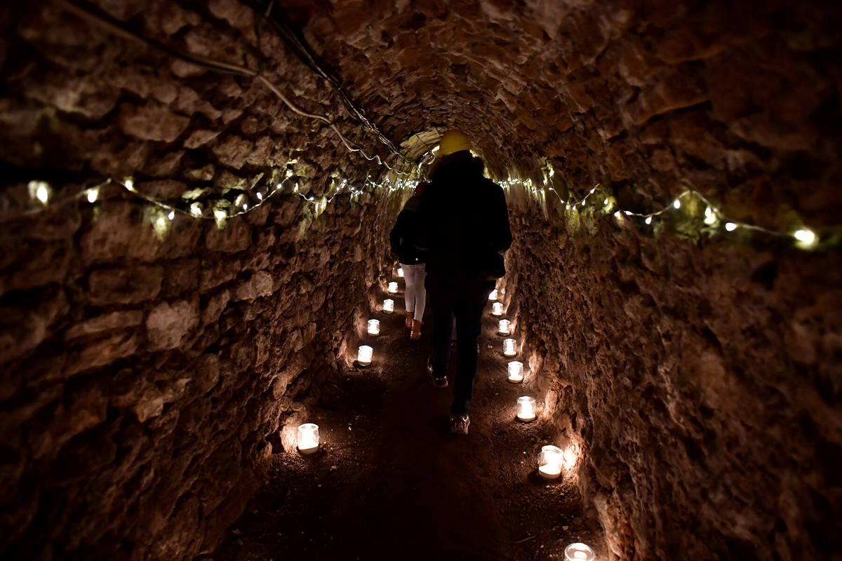 people wandering along a narrow old mining cavern, lit by candles
