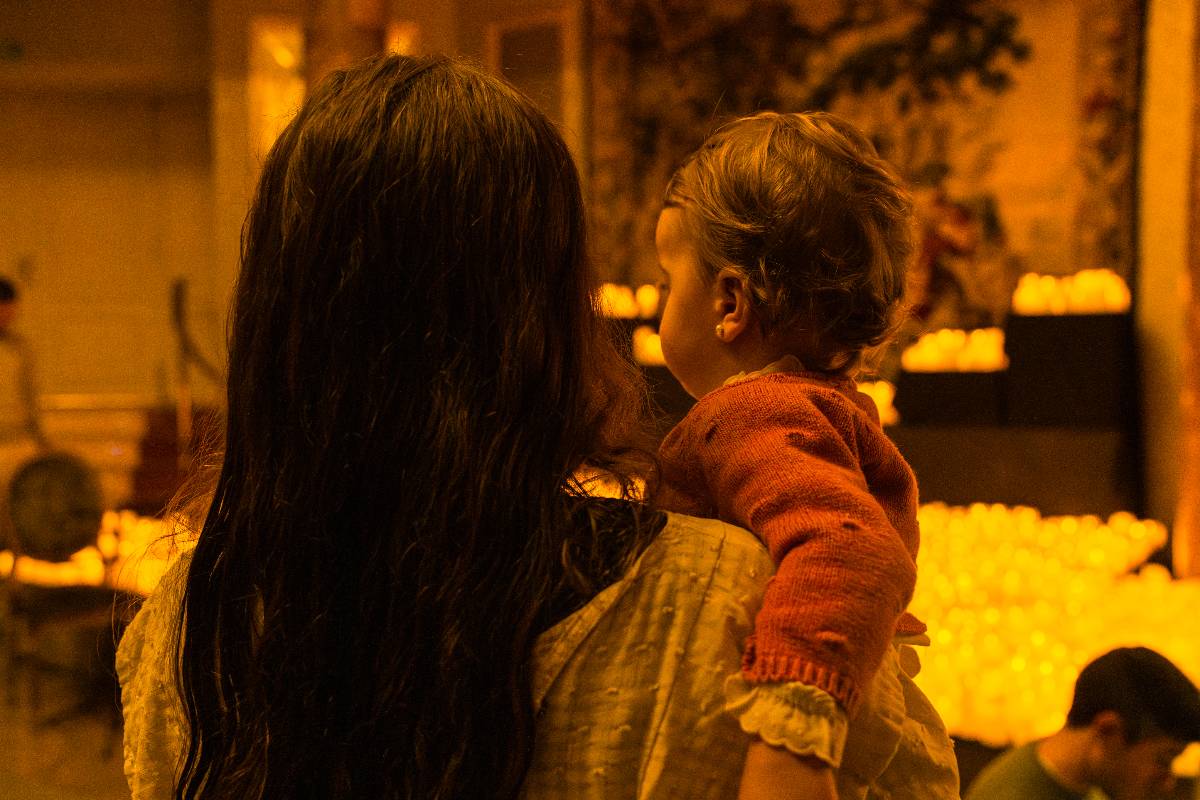 A mother holding her baby to watch the musicians and candlelit stage at Candlelight Babies classical music concert