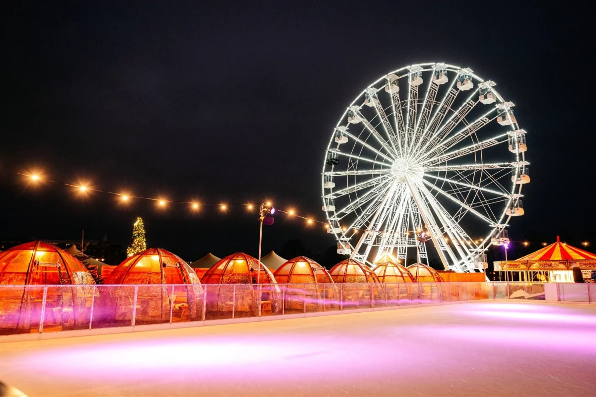 an ice rink and ferris wheel in the background with twinkling chalets at cambridge christmas market