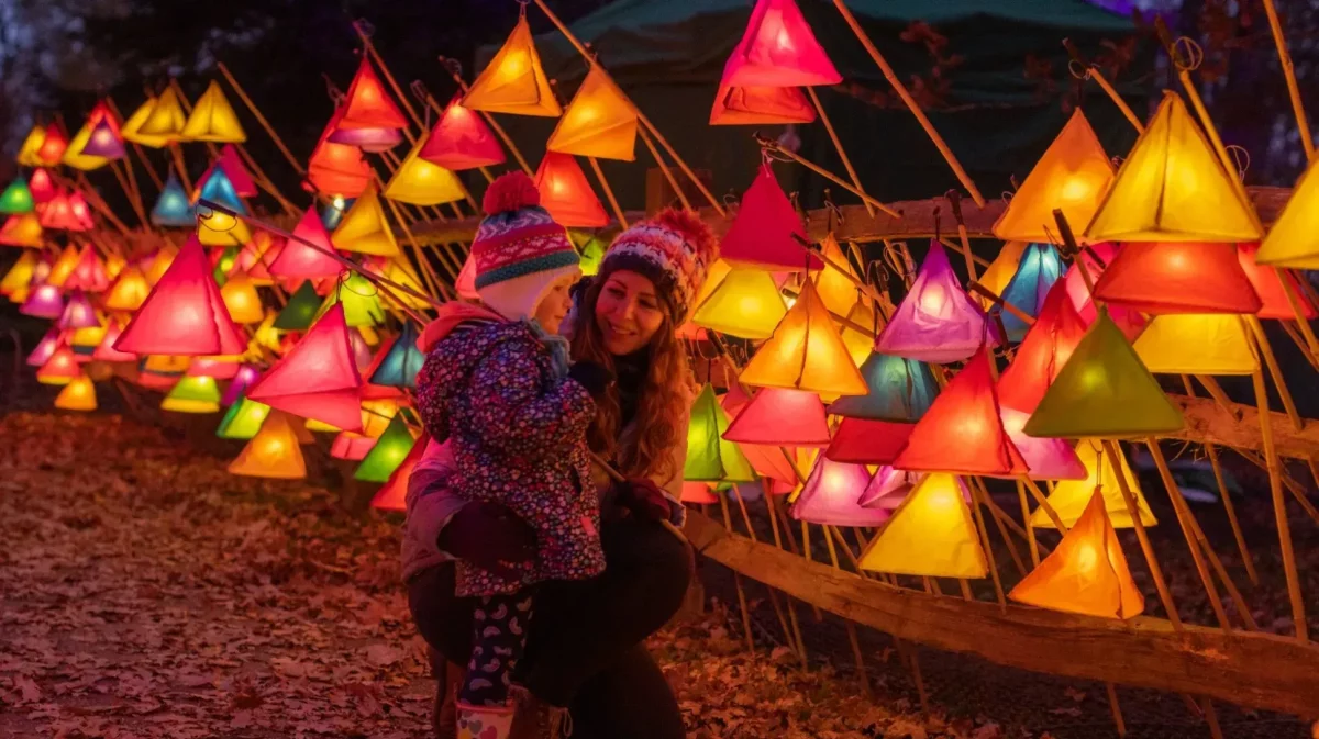 a mother holding their child in front of lit up lanterns at a christmas light trail