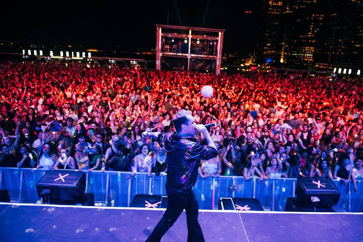 A DJ speaking on stage at a dance party while the crowd watches