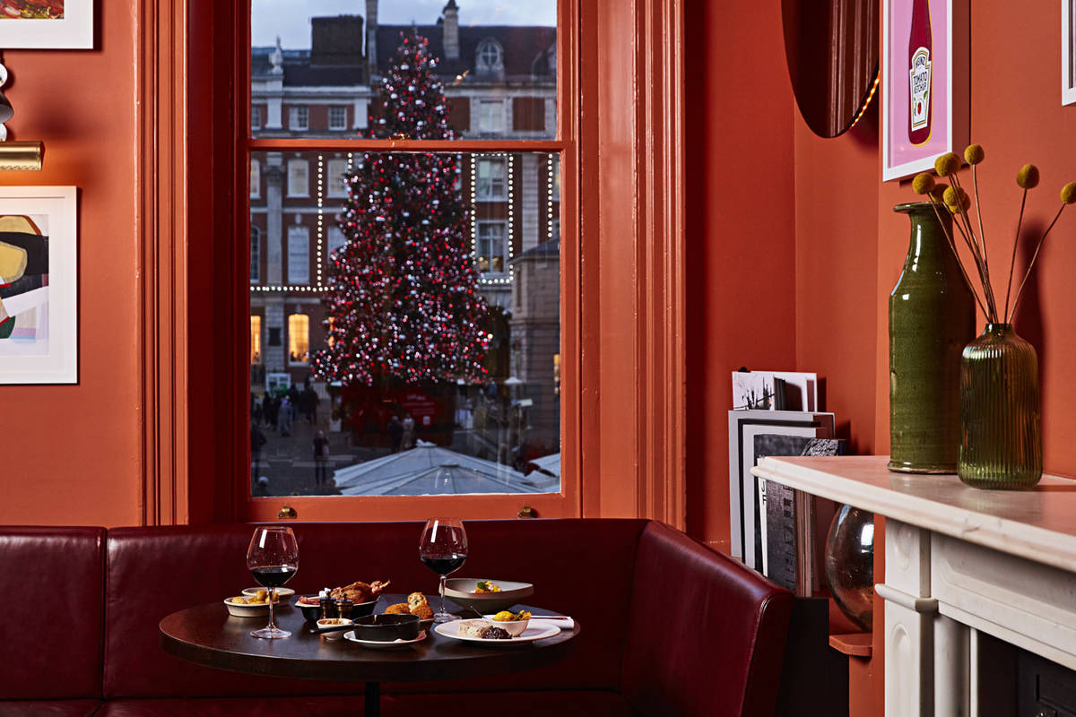 a table set for diners inside the covent garden restaurant pivot, with deep orange walls, and a view out the window behind the table of the covent garden christmas tree