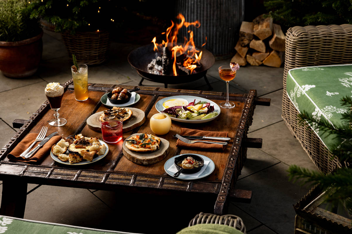a table of food and cocktials next to a roaring fire at a winter rooftop pop-up